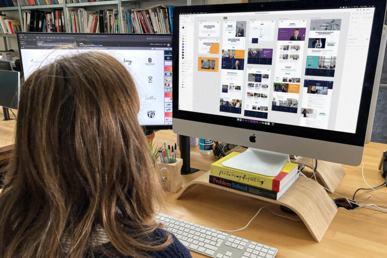 A woman on a computer is seen from behind, page mockups of the Portico website are on the screen