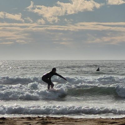 Surfer riding a wave on a sunny day with scattered clouds, near the shoreline.