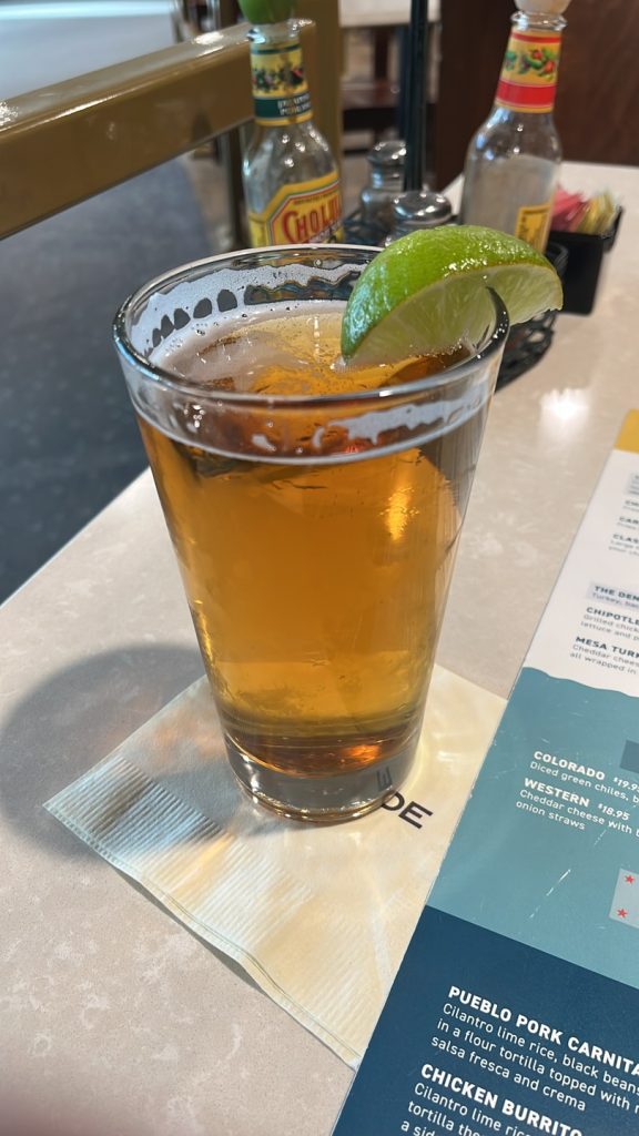 A glass of amber beer garnished with a lime wedge sits on a napkin next to a menu on a table.
