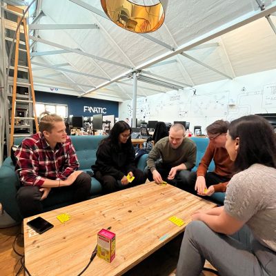 Five people sit around a wooden table with sticky notes and a small game box, in a cozy office space.