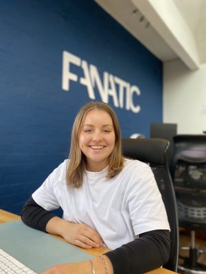 A person smiling while sitting in an office chair, with a blue wall displaying the word 