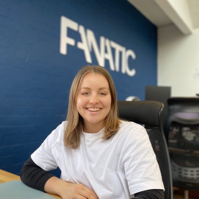 A person smiling while sitting in an office chair, with a blue wall displaying the word 