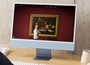 A computer screen displays a website with a chef standing in front of a large framed painting on a burgundy wall.