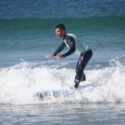 A person in a wetsuit is surfing on a blue surfboard, navigating small waves in the ocean.