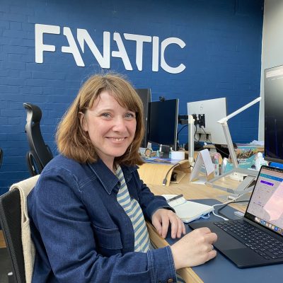 A person smiling at the camera while sitting at a desk with a laptop. The word 
