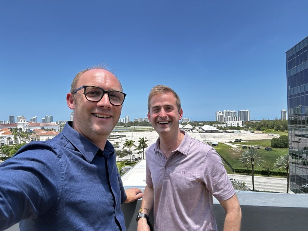 Two people smiling on a rooftop with a cityscape and blue sky in the background.